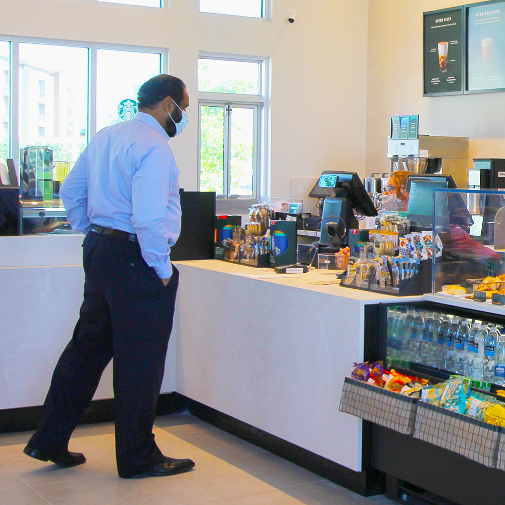Dr. Jamison, vice president for Facilities & Economic Development, wears a mask and keeps his distance as he places an order at the newly-opened Starbucks in Northside at UT Dallas. Anyone teaching, working, or attending classes in person this fall will be required to wear a mask and respect social distancing.