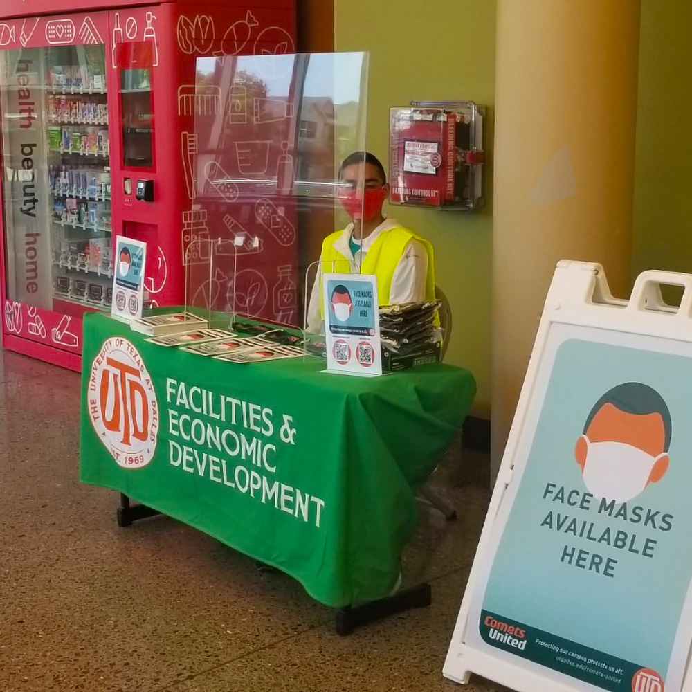 A student ambassador stationed behind a screen outside the University Bookstore in PPE offers free face masks and information on how to help slow the spread of COVID-19 on campus.