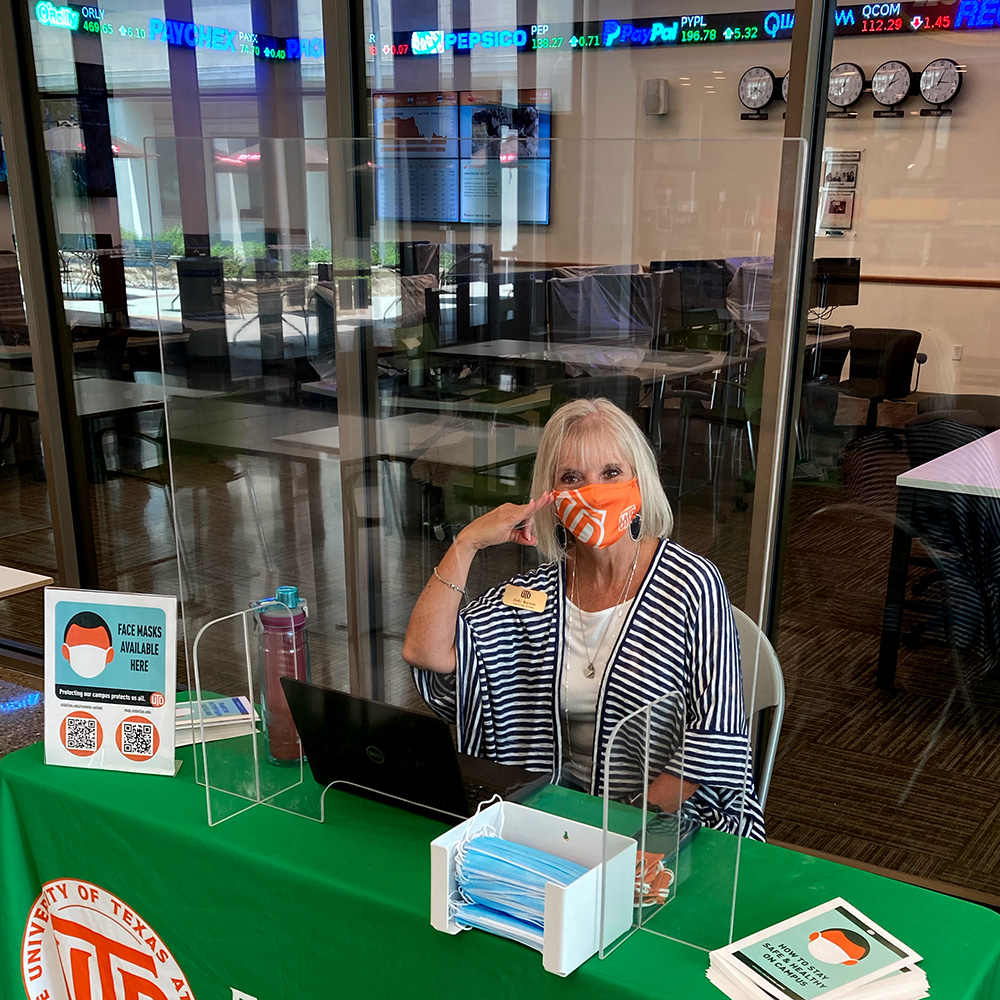 A volunteer in Personal Protective Equipment stationed outside the Naveen Jindal School of Management Trading Lab offers free face masks and information on how to help slow the spread of COVID-19 on campus.