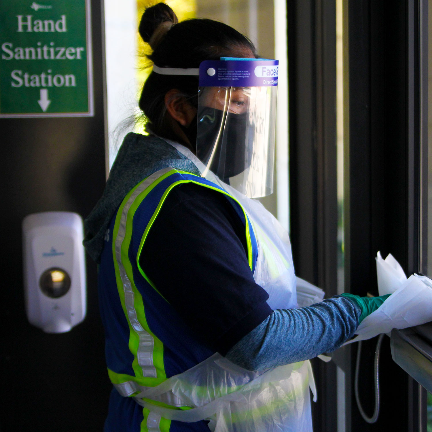 A custodial staff member in Personal Protective Equipment wiping a door handle.