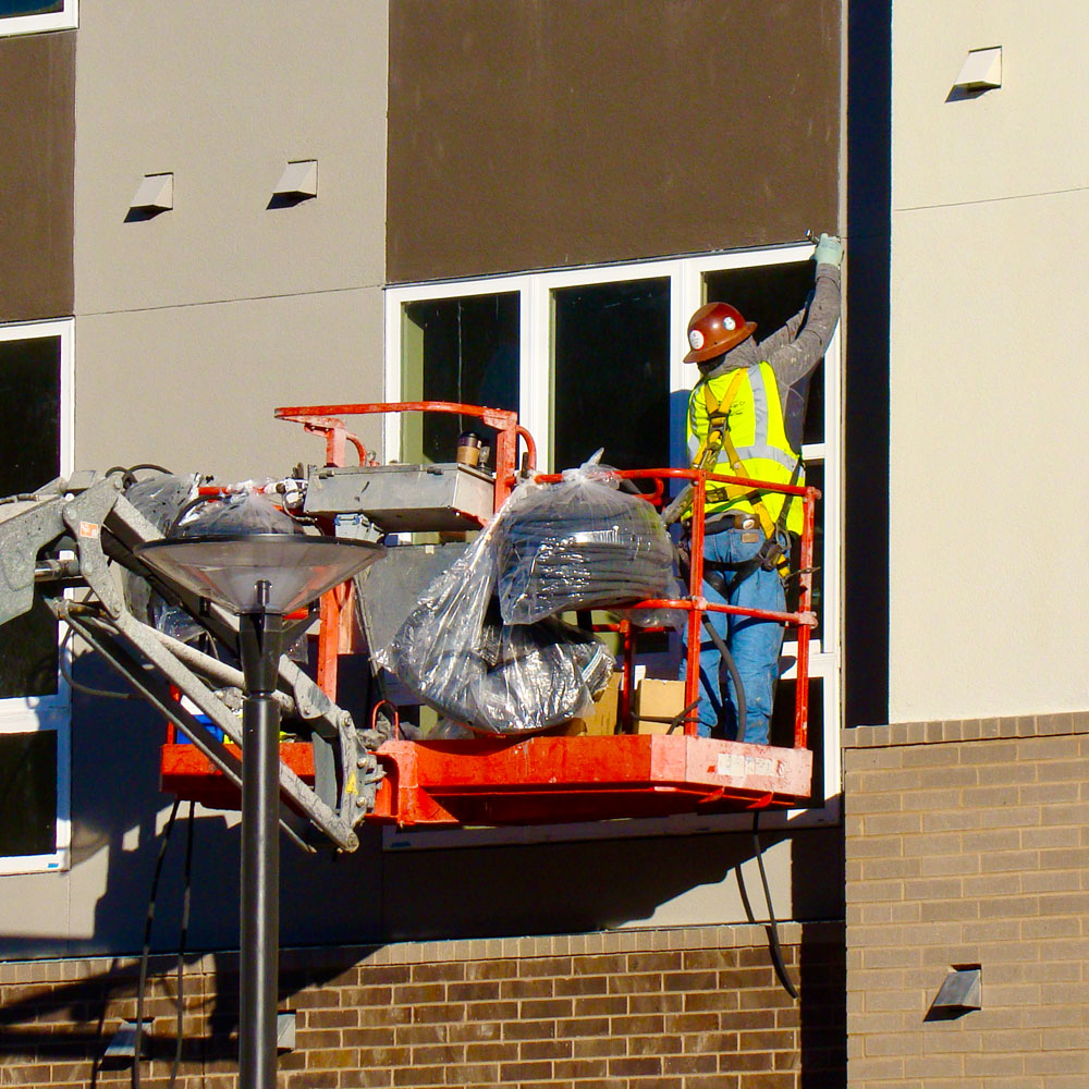 A construction worker stands on a platform to reach a window in the latest addition to Northside at UT Dallas.