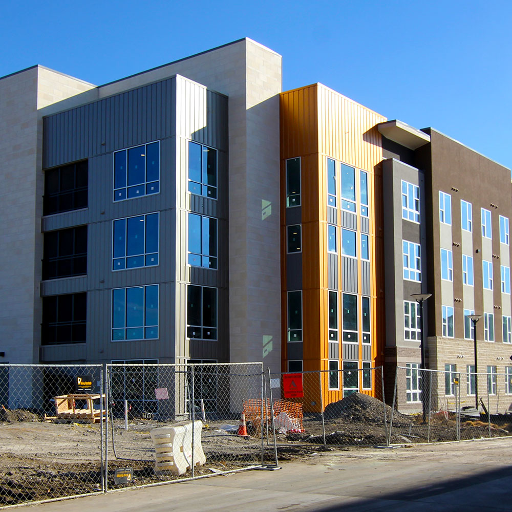 The corner of a building clad in sections of stone, glass, and copper, standing in the middle of a construction zone.