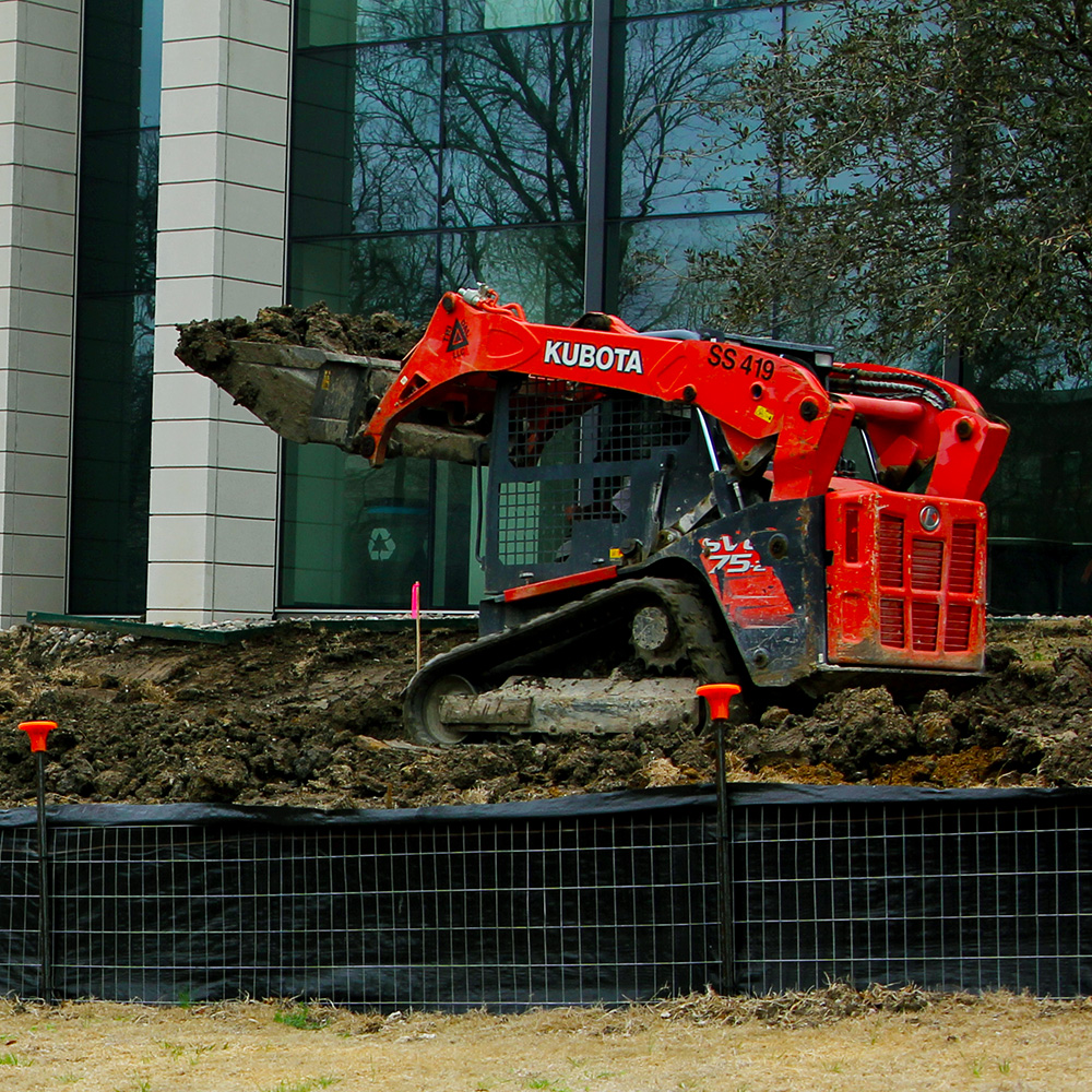 A construction vehicle moves dirt infront of a glass and steel building.