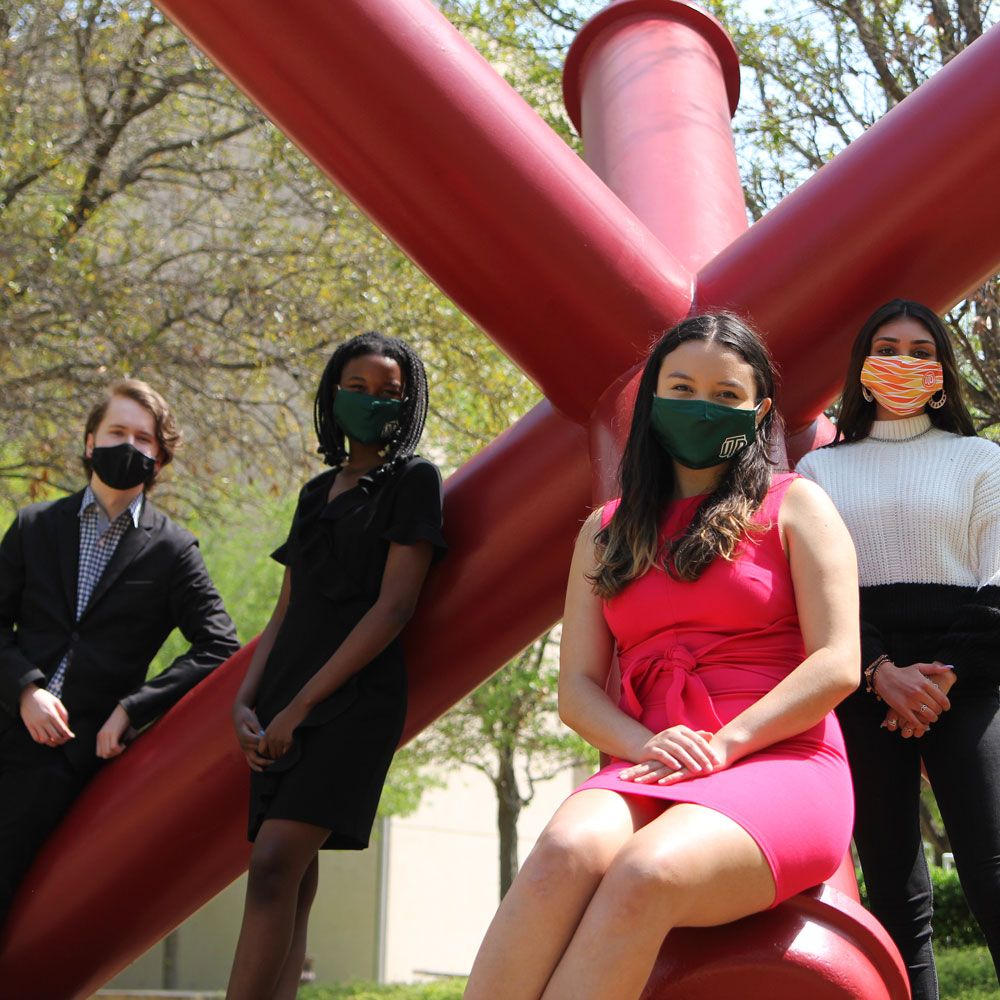 Four students in safety masks pose around a pop art sculpture of a red jack.