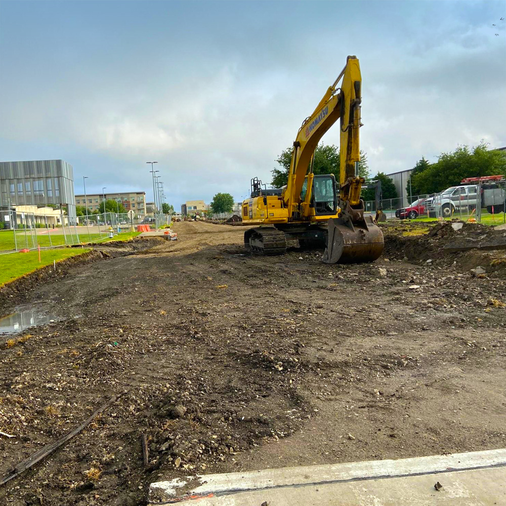 A construction vehicle digs through the dirt in what used to be a paved road.