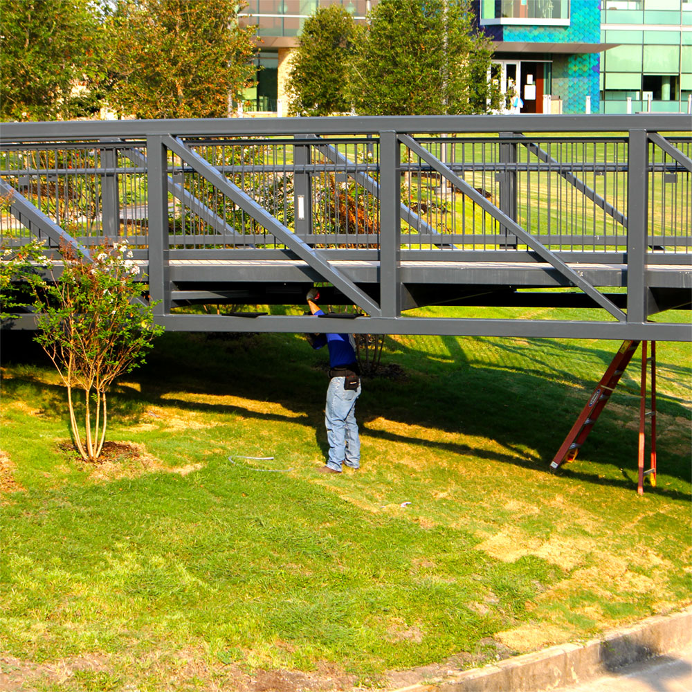 A worker attends to the underside of a black metal bridge.