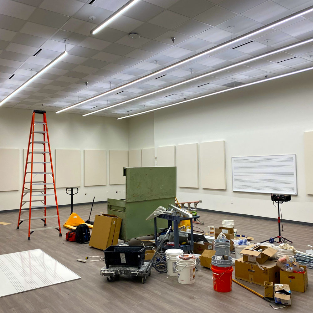 A room paneled in white acoustic tiles, with a whiteboard set up for music notation. Construction supplies sit in the middle of a newly-tiled floor.