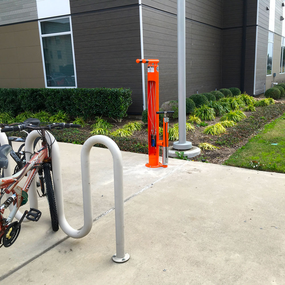 A bike repair station standing between a bike rack and a building.