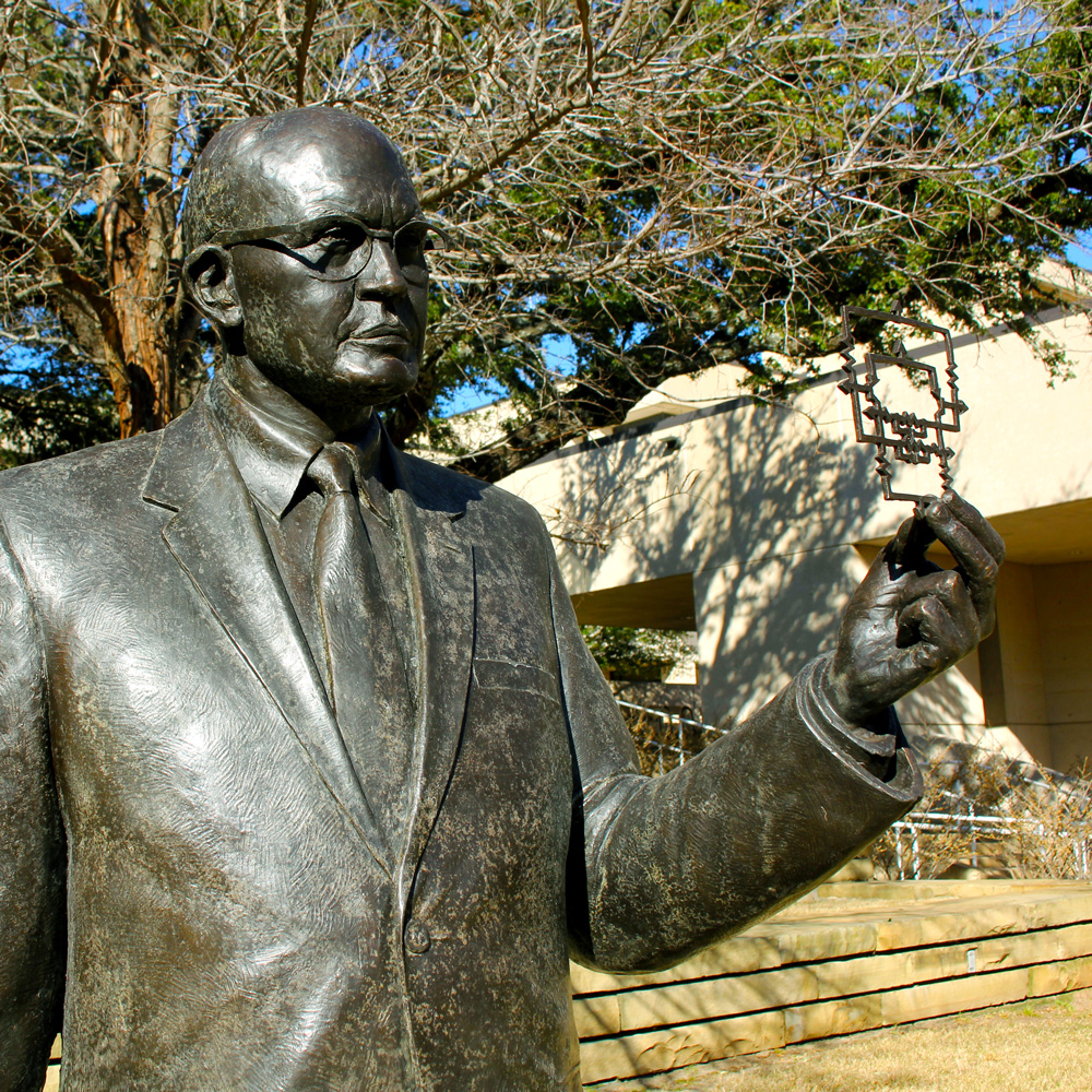 A bronze statue of a man in glasses holding up a circuit diagram.