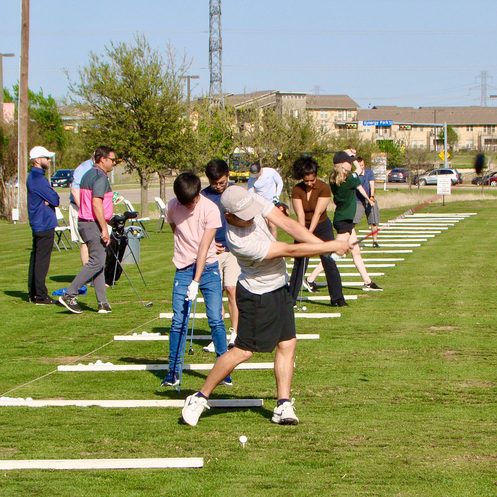 A row of golfers teeing off at a practice range.