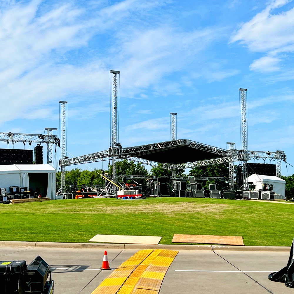 Pieces of scafolding being erected amid large speakers and video screens at the top of a hill.