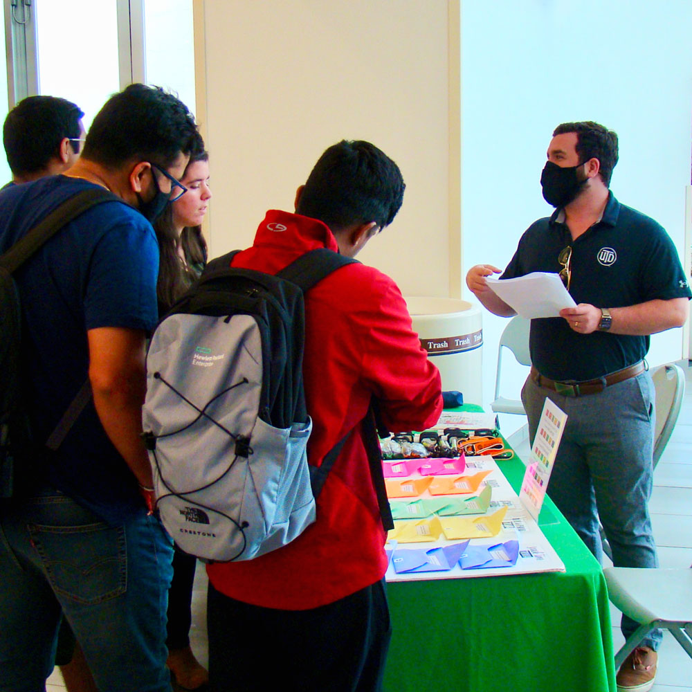 A staff member standing behind a desk answers questions from a group of students.