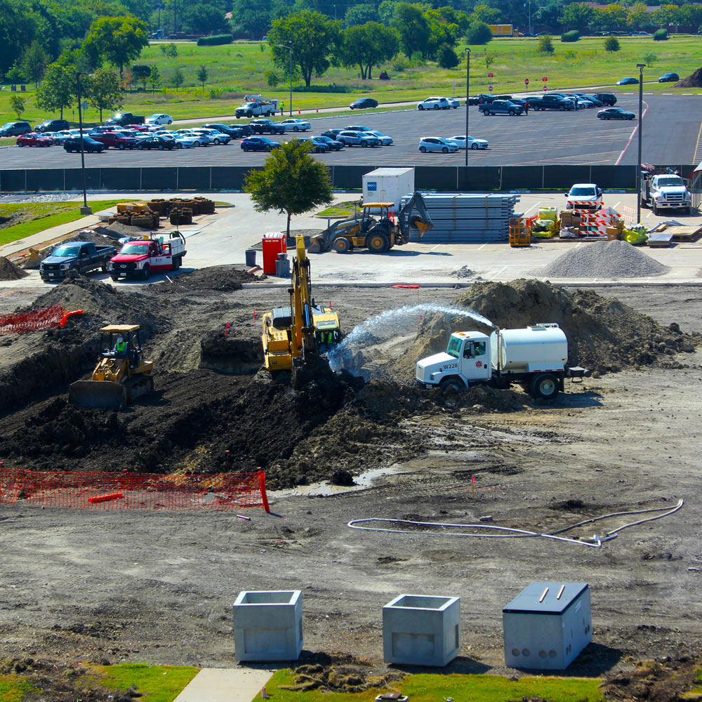 Various pieces of construction equipment dig the beginnings of a foundation.