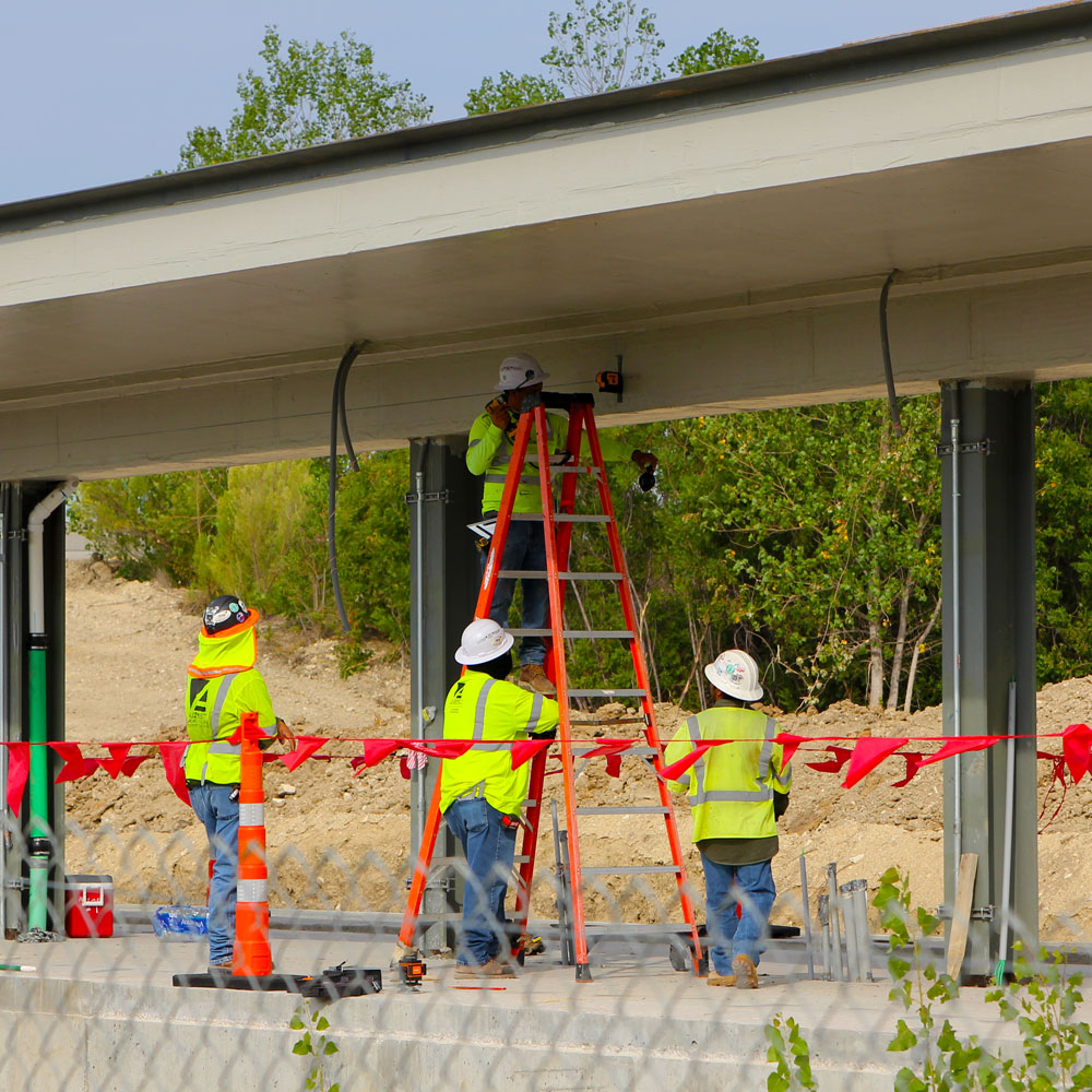 Workers in safety gear measure the dimensions along the underside of a train platform roof.