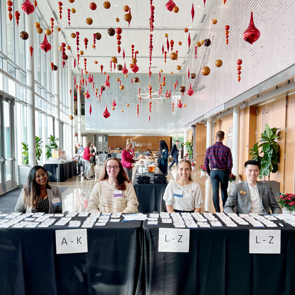 Four people sitting at a registration table in front of a large hallway.