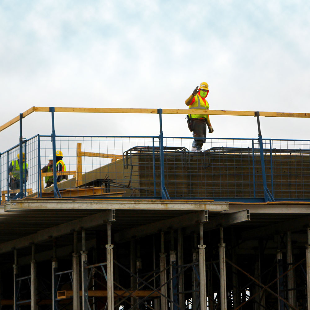 Workers in hard hats and safety vests vests on the roof of a building that is under construction.