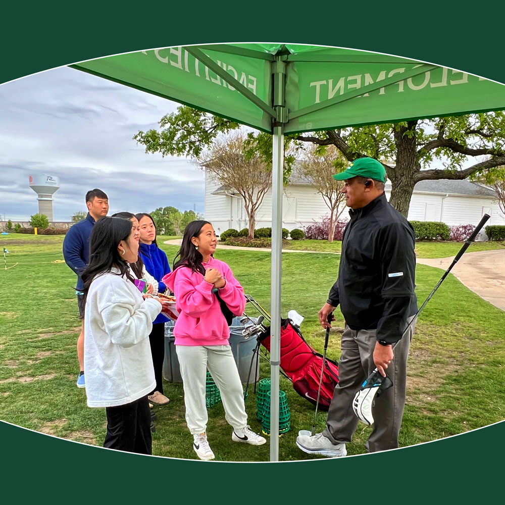 Dr Jamison chats with a group of students on a golf range under a cloudy sky.