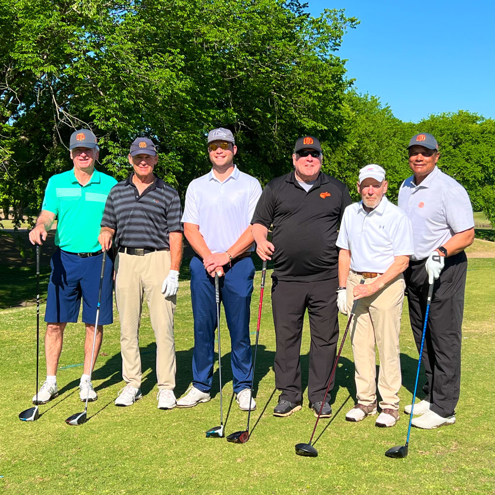 A group of men standing together with their golf clubs on a golf course in a blazing bright day.