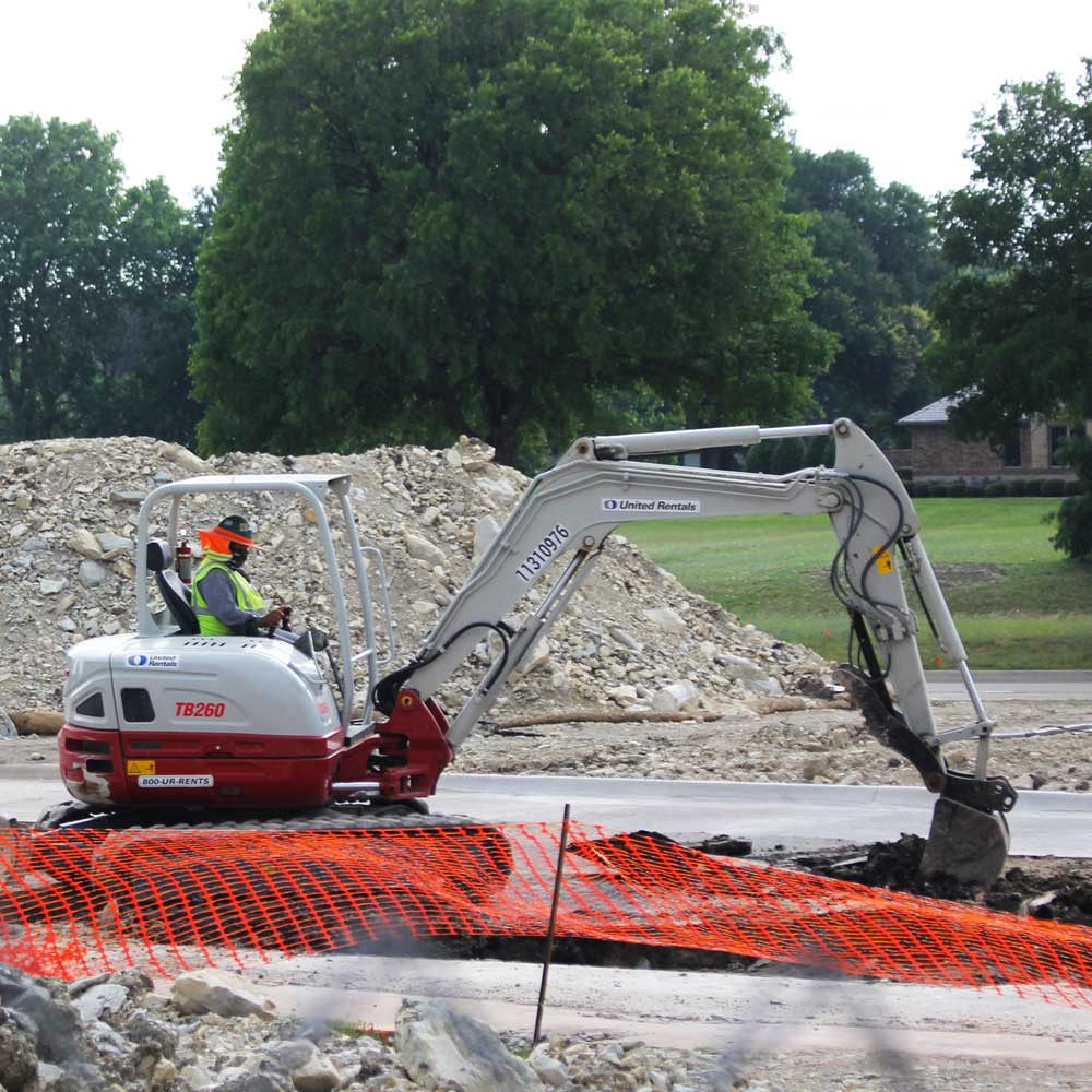 A construction worker breaks through a concrete lot using a compact excavator.