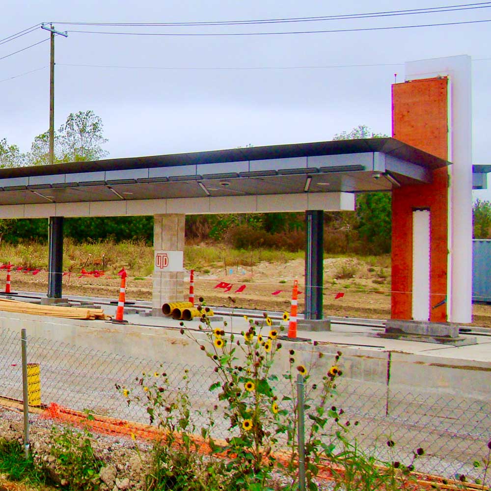 A train platform, under construction. One of the roof pillars bears the UT Dallas monogram logo.
