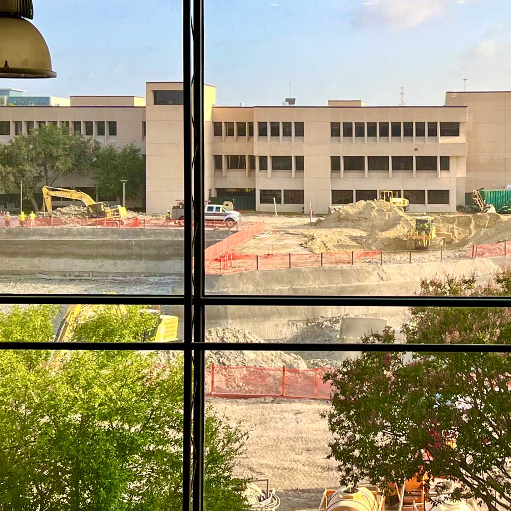 A view of a construction site from a window. Outside the window, a large pit is being excavated.