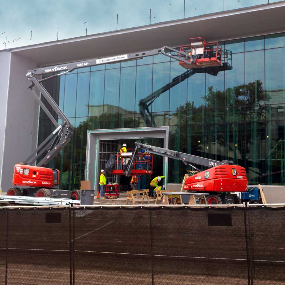 Workers on a pair of cherry-pickers rise up along the glass walls of a building under construction.