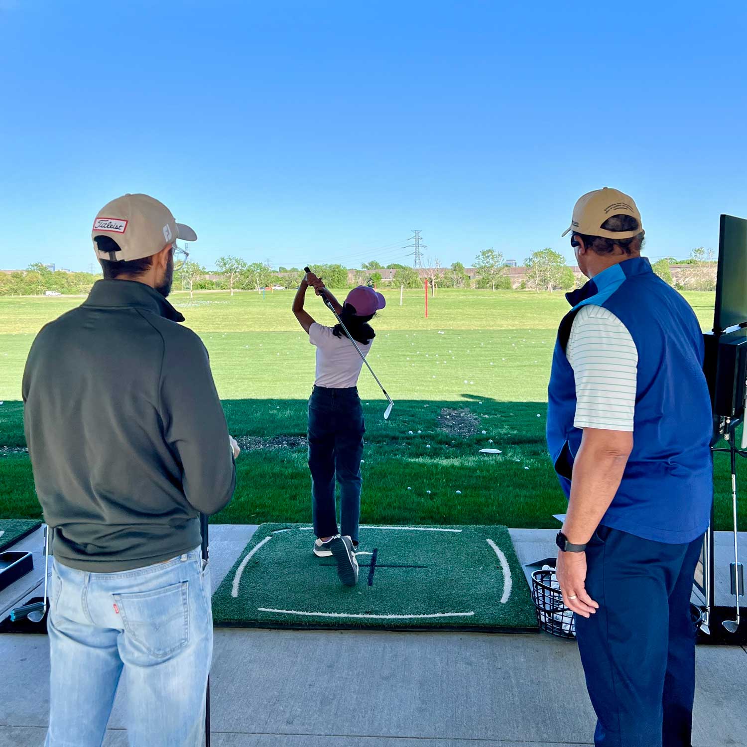 Two golfers look on as a third golfer takes a swing.