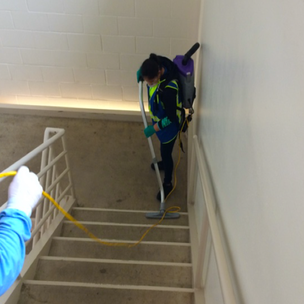 Custodial staff in Personal Protective Equipment disinfecting a stairwell.